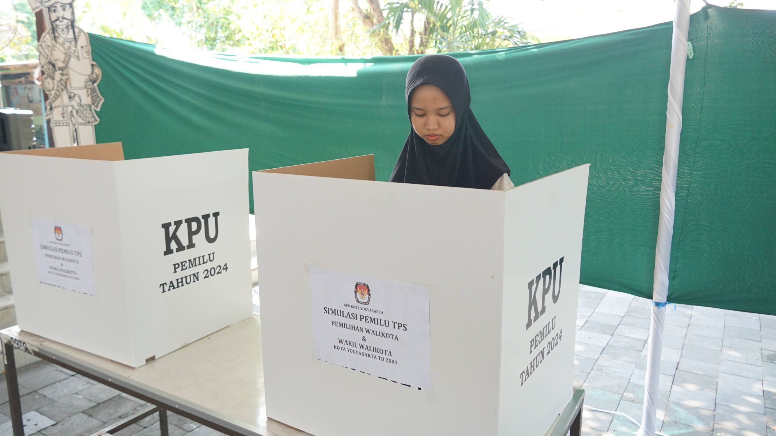 Seorang warga melakukan simulasi menggunakan hak pilihnya dengan mencoblos surat suara di bilik suara. (jogjakota.go.id)